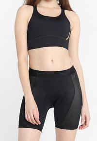 Sujetador deportivo atlético negro con un acabado suave y diseño de espalda cruzada, combinado con pantalones cortos negros ajustados que presentan paneles de malla y una zona acolchada en la parte trasera.