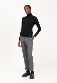 Maglione nero a collo alto in tessuto knit, abbinato a pantaloni grigi a fantasia con pois e scarpe platform nere con dettaglio in catena.