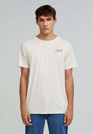 T-shirt en coton crème à manches courtes, avec un petit logo marine sur la poitrine gauche et un col rond classique.