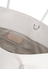 Borsa tote bianca in pelle con superficie testurizzata, dotata di un interno morbido e un'etichetta in pelle con il marchio che recita "Pelle Italiana Autentica".