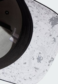 Cappello bianco e nero con una fantasia a spruzzo, realizzato in un tessuto testurizzato e dotato di una fodera in rete. Visiera curvata e dettagli cuciti.