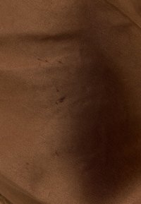 Gros plan d'un tissu marron avec une texture fine tissée, de légères plis et des marques plus foncées discrètes.