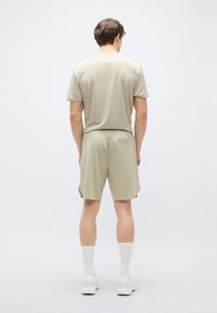 Χακί πουκάμισο με κοντά μανίκια και αντίστοιχο σορτς από ελαφρύ ύφασμα. Το πουκάμισο έχει στρογγυλή λαιμόκοψη· το σορτς διαθέτει ελαστική μέση και πλευρικές σχισμές.