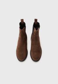Bottines Chelsea en daim marron avec des panneaux élastiques noirs sur les côtés et des tirants. Bout rond et semelles en caoutchouc plates. Design propre et minimaliste.