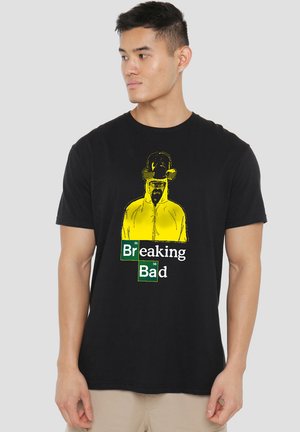 Black cotton t-shirt featuring a yellow graphic portrait and text "Breaking Bad" in green and white, with a relaxed crew neck design.