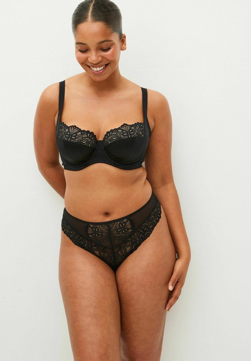 Reggiseno in pizzo nero e culotte a vita alta con motivi floreali. Tessuto liscio con dettagli trasparenti. Spalline regolabili sul reggiseno.