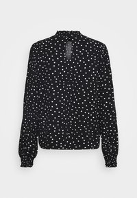 Blusa nera con pois bianchi, maniche lunghe a sbuffo, scollatura arricciata e dettaglio a goccia sulla schiena. Realizzata in tessuto leggero.