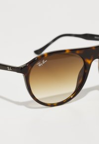 Ochelari de soare tortoise cu lentile degradate de culoare maro. Au rame rotunde și accente din metal. Logo-ul Ray-Ban este plasat pe ramă.