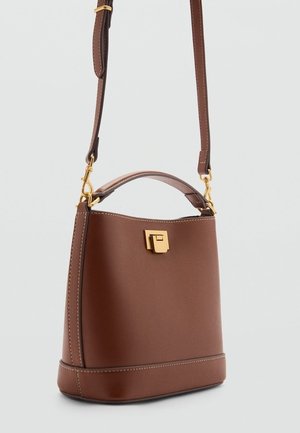 Sac à main en cuir marron avec fermoir doré, bandoulière réglable et poignée supérieure, posé debout sur un fond clair uni.