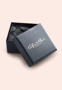 Schwarze Schmuckschatulle mit strukturierter Oberfläche und weißem aufgedrucktem Logo, leicht geöffnet, mit dunklem, zerknittertem Papier im Inneren.