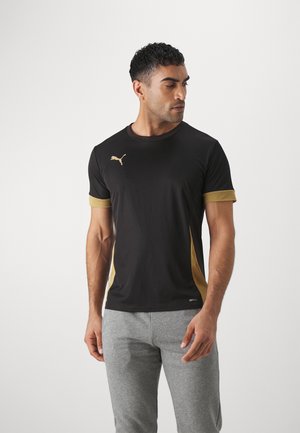 Sort trænings-t-shirt med guld accenter på ærmerne og siderne, med et lille logo på brystet. Fremstillet af fugttransporterende materiale.