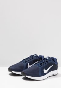 Baskets de course bleu marine avec tige en mesh, logo swoosh blanc, semelle extérieure en caoutchouc noir et épaisse semelle intermédiaire blanche. Présente un système de laçage.