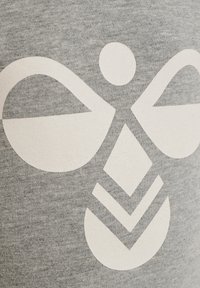 Grå t-shirt med en stor vit grafisk design bestående av abstrakta former, inklusive en cirkel och en diamant, på ett texturerat tyg.