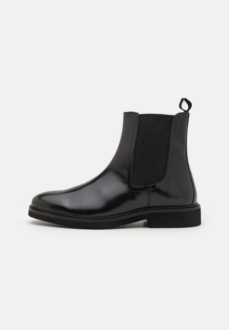Botas Chelsea negras de cuero brillante, con paneles laterales elásticos, una lengüeta y una suela de goma plana.