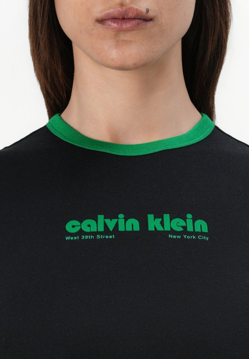Schwarzes T-Shirt mit grünem Rippkragen. Mit "calvin klein" und "West 39th Street, New York City" in fettem grünen Schriftzug bedruckt.