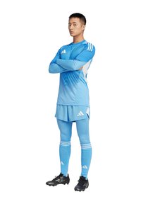 Completo da calcio azzurro chiaro con maniche lunghe e pantaloni coordinati, caratterizzato da un motivo a gradiente, tre strisce bianche sulle spalle e scarpe da calcio nere.