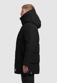 Svart puffjacka med huva, med horisontella quiltade sektioner, dragkedjefickor och en texturerad krage. Tyget är slätt och matt.