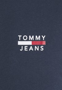 Námořnická tkanina s bílým a červeným logem Tommy Jeans s blokovými písmeny a horizontálním barevným pruhem mezi slovy.