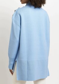 Suéter de punto azul claro con cuello alto, puños acanalados y aberturas laterales. Presenta detalles de botones en el hombro para un toque adicional.