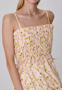 Robe smockée florale rose avec des fines bretelles, présentant un bustier ajusté et une jupe fluide ornée de motifs de feuilles jaunes.