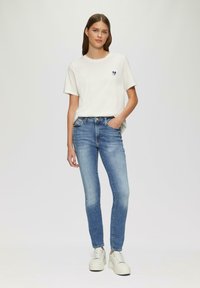 Camiseta de algodón de color claro con un diseño de corazón, combinada con jeans ajustados azules. El calzado incluye zapatillas de plataforma blancas.