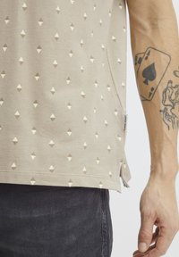 Beige színű pamut ing, strukturált felülettel, apró barna és fehér háromszögekből álló geometrikus mintával. Oldalsó hasítékok a megfelelő illeszkedés érdekében.