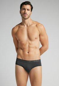 Schwarze Herrenunterhosen aus glattem, dehnbarem Material mit einem bedruckten Bund und einem taillierten Design, das einen minimalistischen Stil betont.