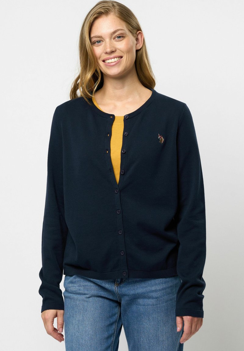 Cardigan bleumarin cu mâneci lungi, decolteu rotund și închidere cu nasture. Prezintă un mic detaliu brodat pe pieptul stâng.