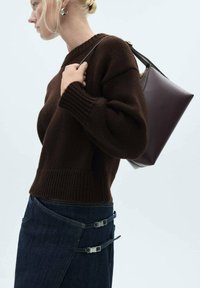 Brauner gestrickter Pullover mit gerippten Bündchen, kombiniert mit einem dunklen Jeansrock mit silbernen Hardware-Akzenten und einer burgunderfarbenen Handtasche.