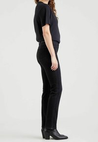Mustat farkut slim fit -mallilla, korkealla vyötäröllä ja sivutaskuilla, yhdistettynä lyhythihaiseen mustaan toppiin ja mustiin nilkkabootseihin, joissa on korkoa.