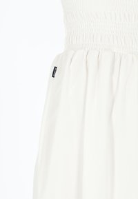 Witte jurk met een gesmockte lijfje, vloeiende rok en een label aan de linkerkant. Glad, lichtgewicht stof met een subtiele textuur.