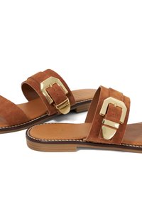 Bruine suede sandalen met een brede band en een gouden gesp. Vlakke zool met een gestikte rand. Soepele leren inlegzool.
