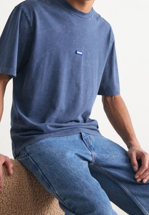 Marineblauwe katoenen t-shirt met korte mouwen, ronde hals en een klein blauw "HUGO" logo op de borst, gecombineerd met lichtblauwe jeans.