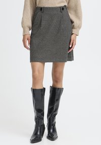 Skørt med ternet houndstooth-mønster i sort og hvidt, med frontfolder og to knapper, parret med høje sorte læderstøvler.