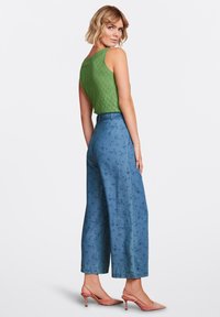 Grön stickad ärmlös topp kombinerad med högmidjade, vida blå byxor med ett subtilt mönster. Rosa klackar fulländar outfiten.