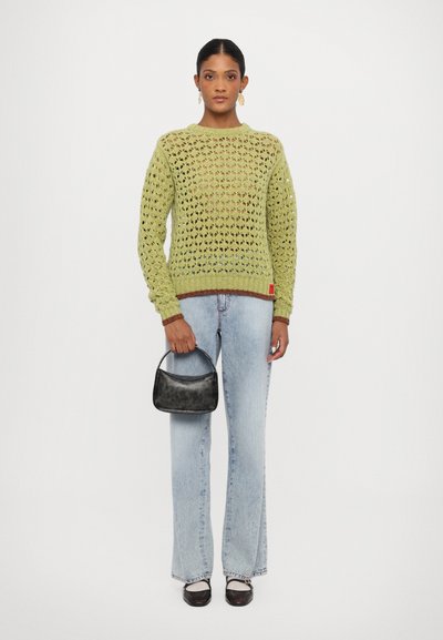 Pull en tricot vert lime avec un motif ajouré, col rond et poignets côtelés, associé à un jean évasé bleu clair et un petit sac à main noir.