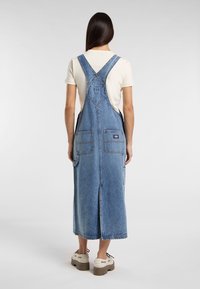 Vestido de tirantes de mezclilla, color azul claro, con tirantes ajustables, dos bolsillos frontales, una apertura en la parte trasera y un corte relajado.