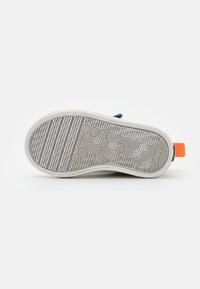 Podeszwa dziecięcego sneakersa z heksagonalnym i paskowanym wzorem bieżnika, z białą obwódką i pomarańczową pętelką na pięcie.