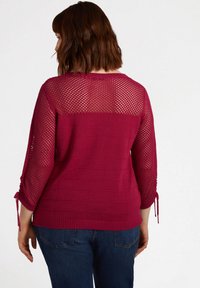 Magenta långärmad tröja med en texturerad öppen stickad rygg, ribbad nederkant och justerbara knytband på ärmarna. Slätt, mjukt tyg genom hela plagget.