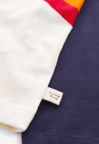 Majica s kratkimi rokavi iz kremastega in mornarsko modrega bombaža, z etiketo z napisom "Little Bird." Gladek otip, sproščen kroj, minimalističen dizajn.