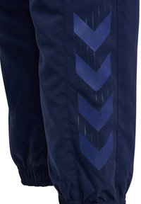 Nahaufnahme eines marineblauen Hosenbeins mit elastischem Bündchen und vier dunkelblauen Chevron-Streifen, die vertikal verlaufen.