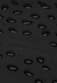 Fekete vízálló felület vízcseppekkel, textúrált mintázattal és dombornyomott "JOHNNY URBAN" logóval. Általános sima felület.