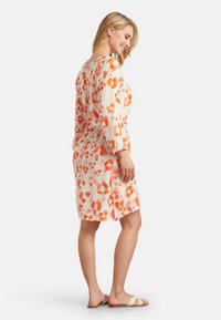 Floral dress made of lightweight fabric, featuring orange and coral splotches on a cream background, mid-length with long sleeves and a relaxed fit.