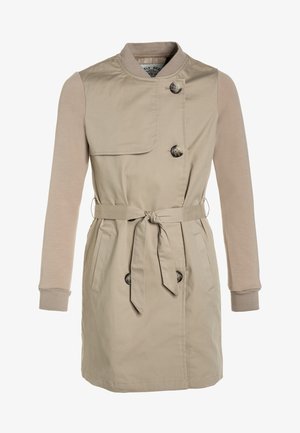 Manteau beige en trench avec un col rond, fermeture à boutons, manches longues et taille ceinturée. Le tissu combine des textures lisses et tricotées.