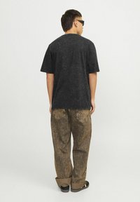 Sort t-shirt med korte ærmer og struktureret overflade, parret med løstsiddende brune mønstrede jeans og sorte sko, set fra ryggen.