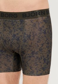 Sötétzöld boxernadrág fekete gumis derékkal, amelyen a "BJÖRN BORG" felirat található. Texturált minta különböző zöld és fekete árnyalatokban.