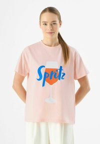 Roze katoenen T-shirt met een afbeelding van een drankje in een glas, voorzien van de tekst "Spritz" in het blauw. Korte mouwen en een relaxte pasvorm.