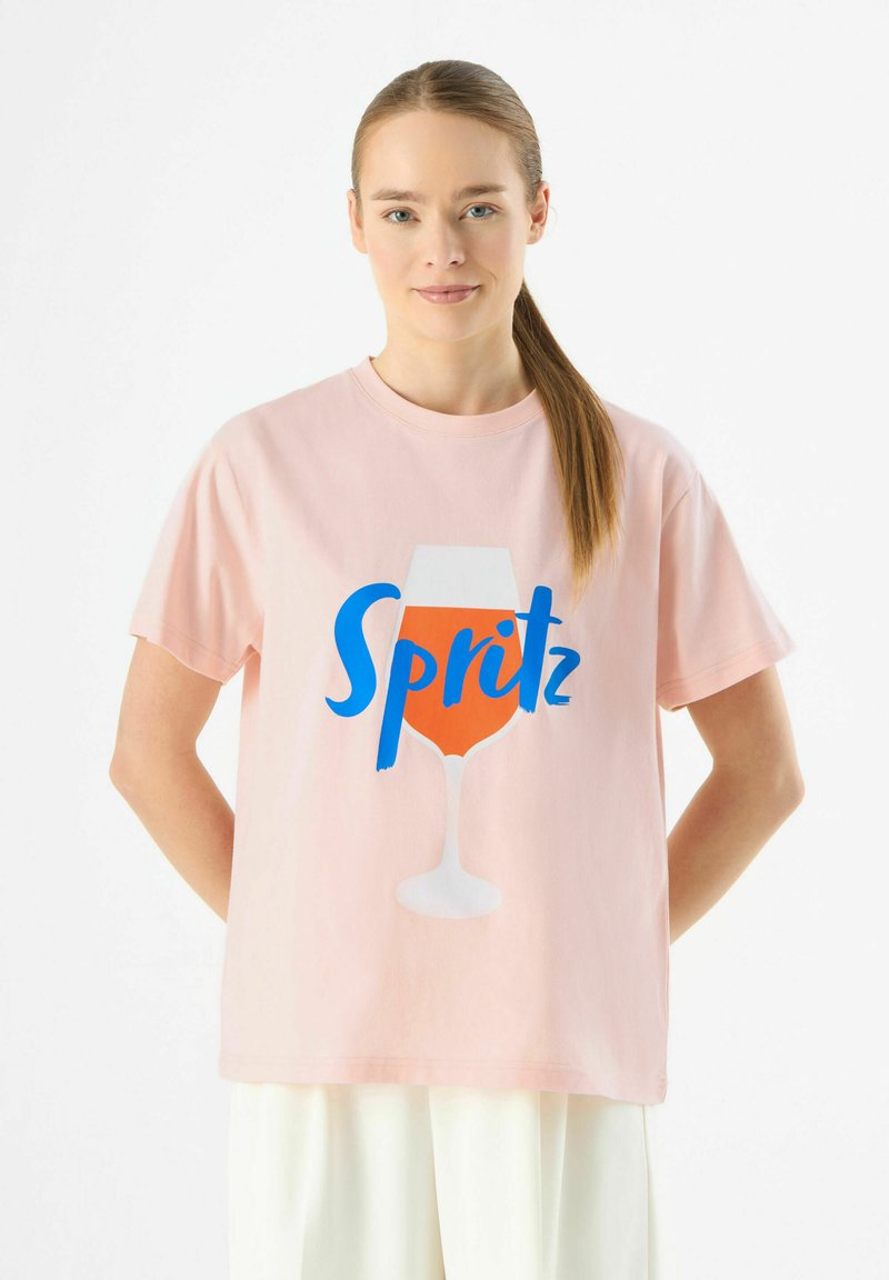 Roze katoenen T-shirt met een afbeelding van een drankje in een glas, voorzien van de tekst "Spritz" in het blauw. Korte mouwen en een relaxte pasvorm.