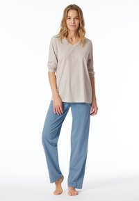 Hellgraues, gemustertes Langarmoberteil mit V-Ausschnitt und hochgekrempelten Ärmeln, kombiniert mit locker sitzenden blauen Hosen, bodenlang und mit glatter Textur.