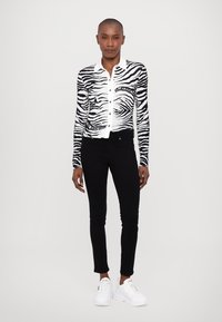 Cárdigan de estampado de cebra en blanco y negro con mangas largas y botones delanteros, combinado con jeans skinny negros y zapatillas blancas.